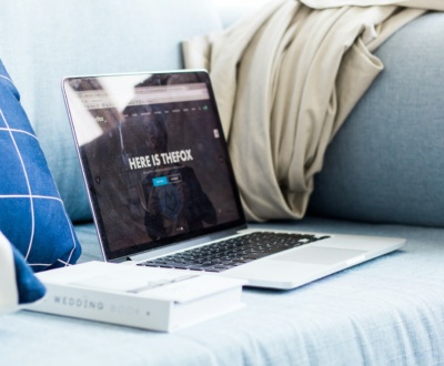 A laptop sitting next to a book on a couch.